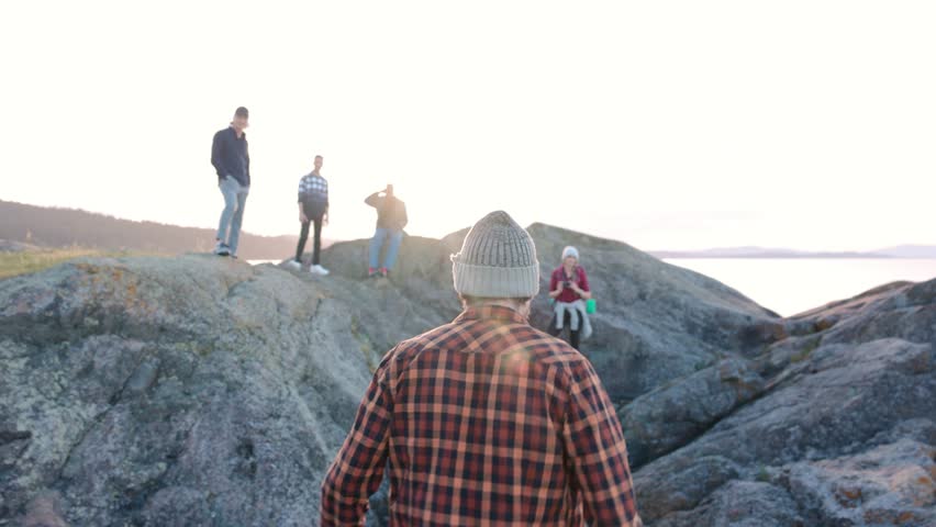 Friends watching man walking over fallen tree on rocks