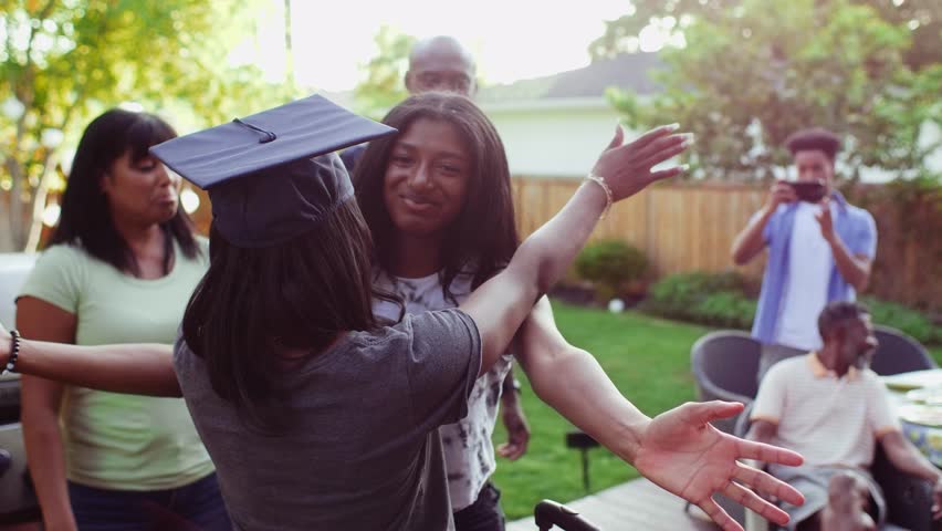 Teenage girl hugging high school graduate sister on patio