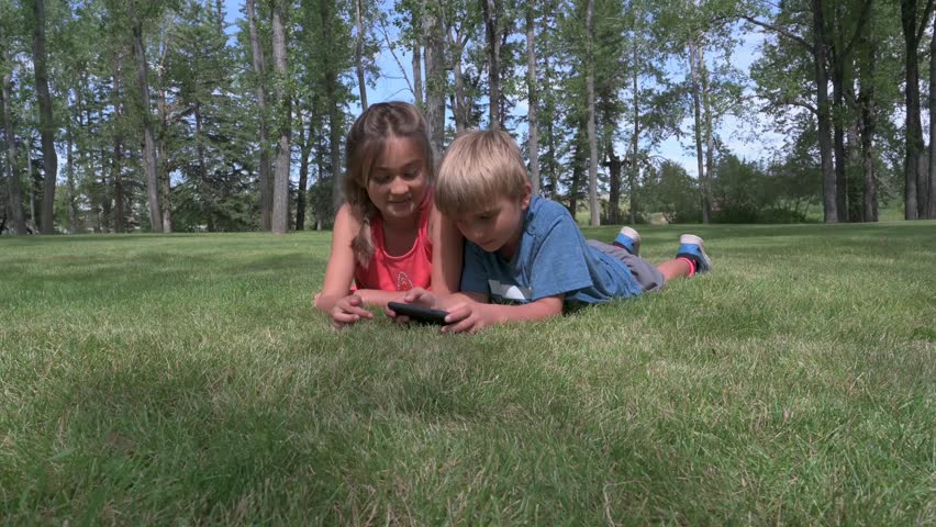 Boy and girl lying on grass with smartphone
