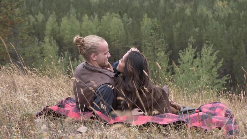 Affectionate couple cuddling on blanket on rural mountainside