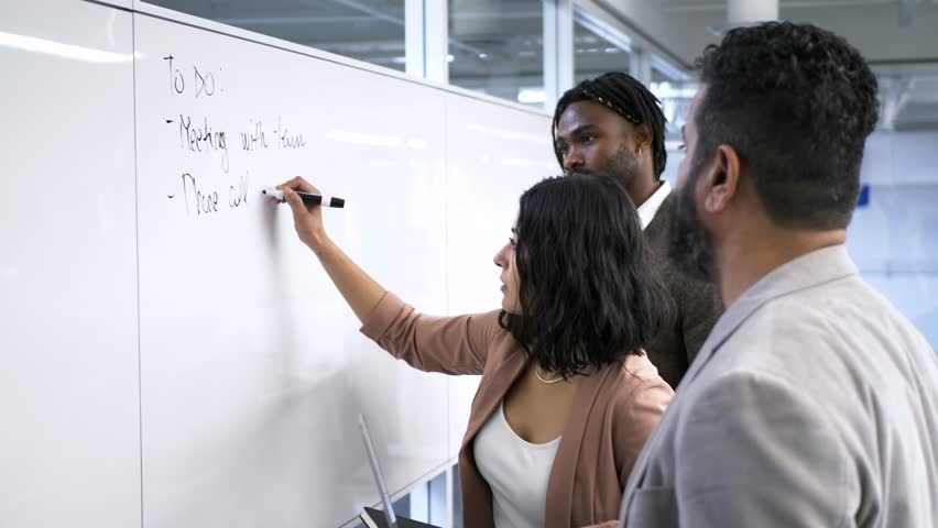 Business people writing to do list on whiteboard in office meeting