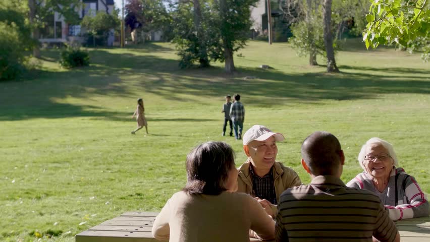 Happy multigenerational family talking at picnic table in sunny park