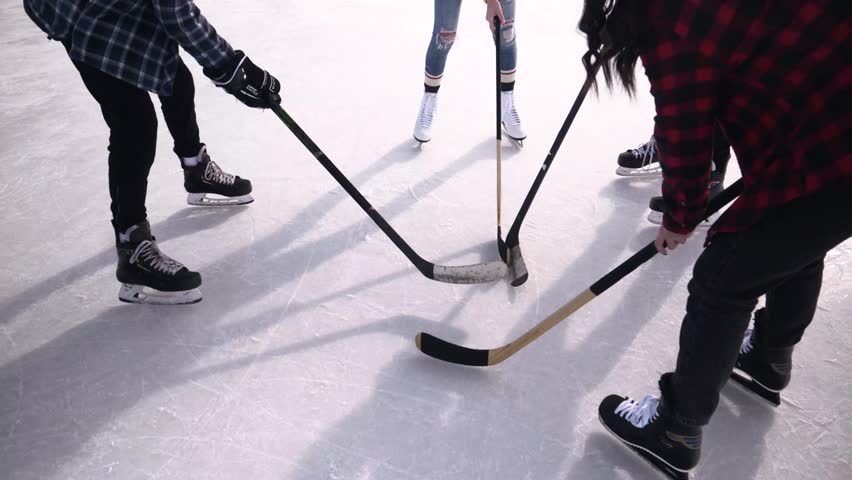 Teenage friends playing ice hockey on sunny outdoor winter ice rink