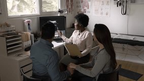 Female doctor discussing ultrasound with pregnant couple in exam room - Powered by Shutterstock - Get 15% off with code: PIKWIZARD15