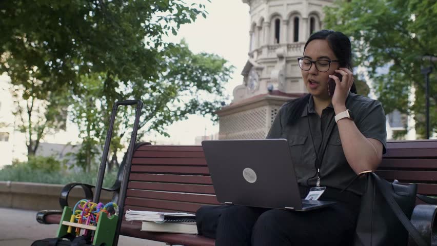 Cheerful saleswoman working with digital devices on park bench