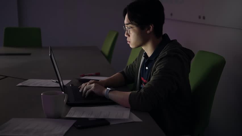 Businessman looking at smart watch working late at laptop in conference room