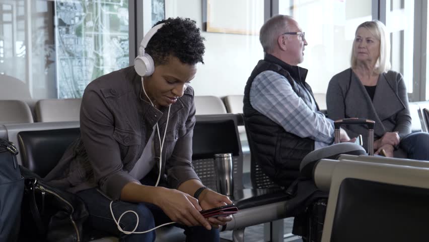 Woman with headphones and smart phone waiting in airport
