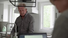 Senior man doing dishes while wife uses laptop in kitchen - Powered by Shutterstock - Get 15% off with code: PIKWIZARD15