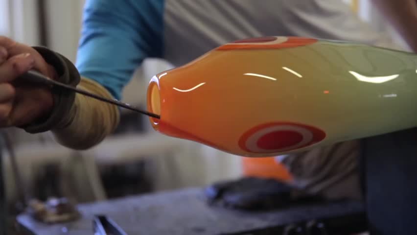 Glass blower rolling and shaping glass with tongs