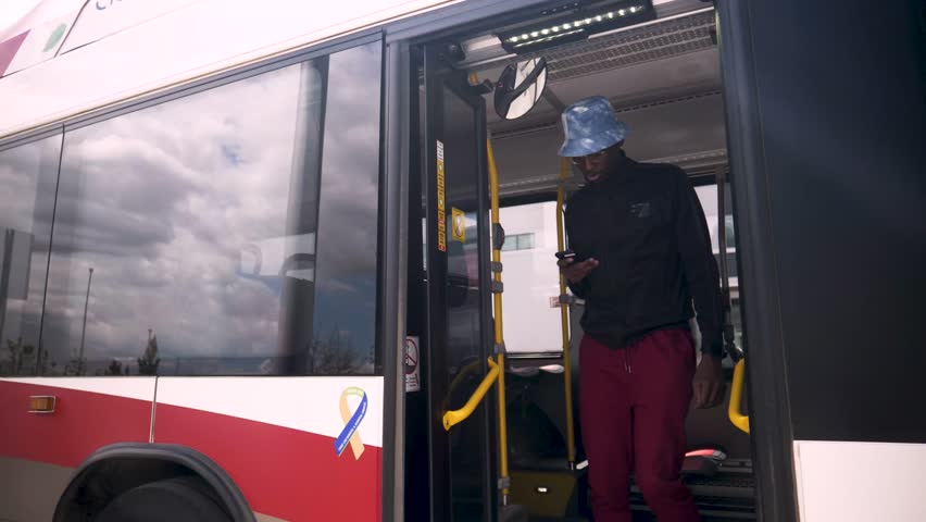 Young man with smart phone getting off public transit bus