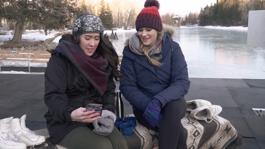 Young women friends taking selfie at ice skating pond in winter park