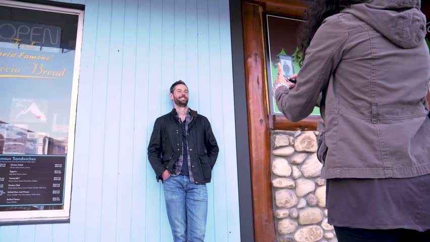 Slow motion of woman taking photo of man in front of blue panel
