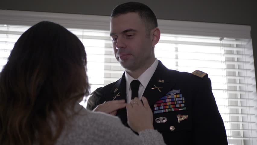 Wife helping military officer husband with formal uniform jacket