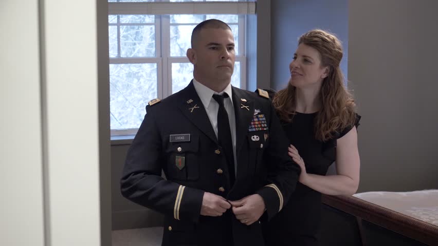 Wife helping male officer get dressed in formal uniform