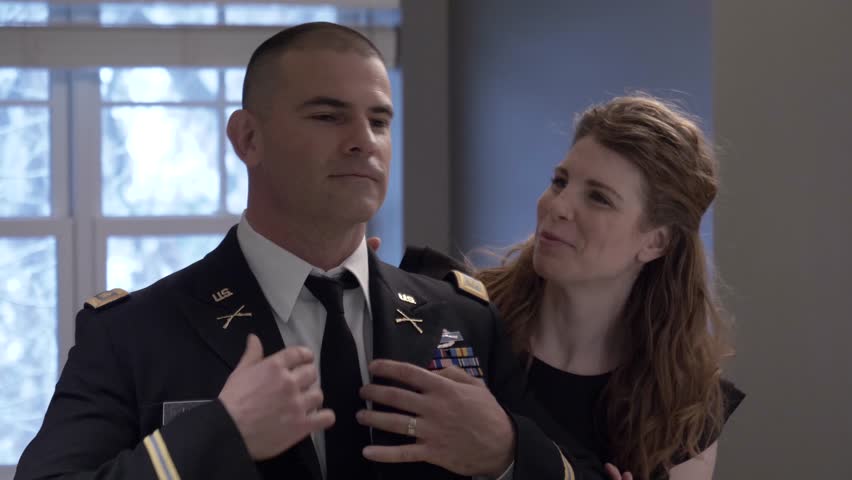 Wife helping officer husband put on formal military uniform