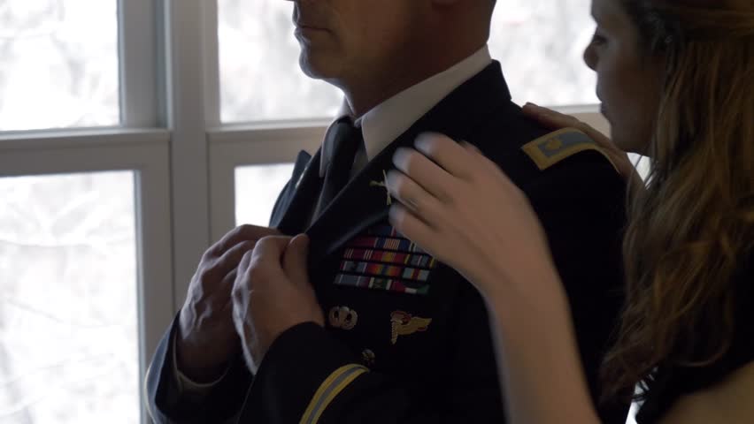 Wife helping officer husband with formal military uniform