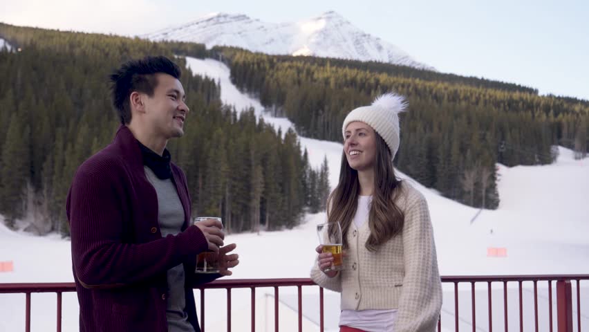 Snowboarder couple taking and drinking beer on snowy mountain patio