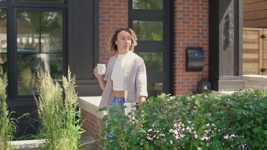 Young woman walking and drinking coffee outside house