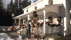 Slow motion of couple hanging Christmas lights on house in snow - Powered by Shutterstock - Get 15% off with code: PIKWIZARD15