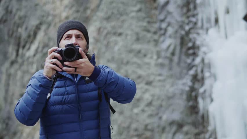 Slow motion of man taking photo of frozen waterfall