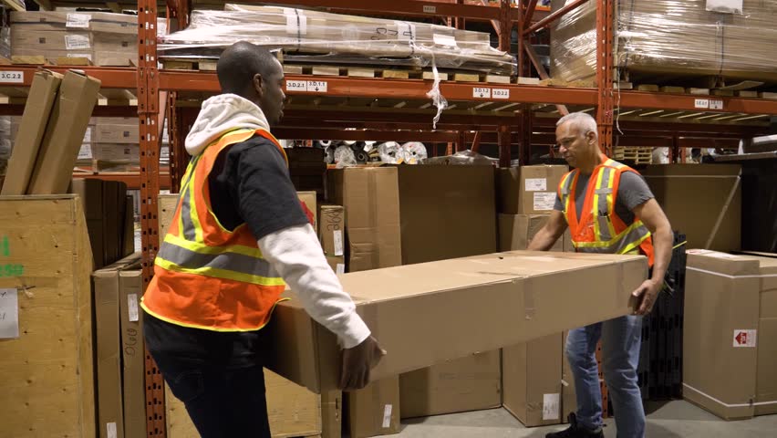 Male warehouse workers placing large cardboard box below shelf