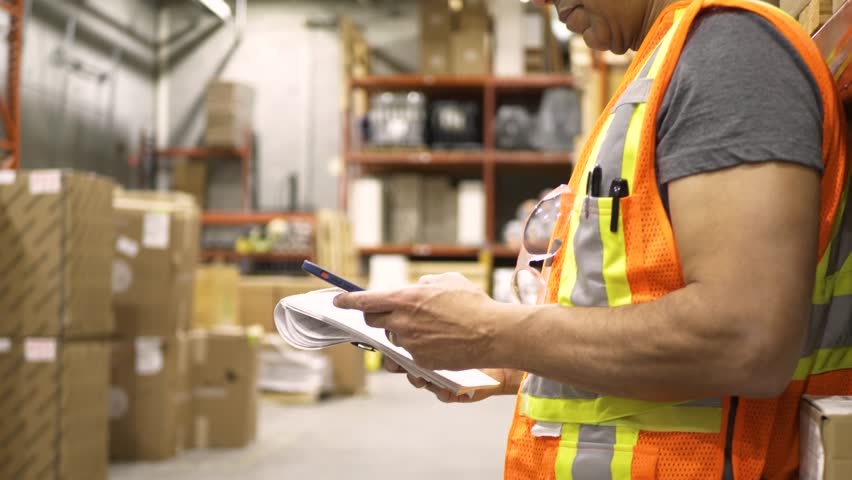 Male supervisor with smart phone and notepad in warehouse