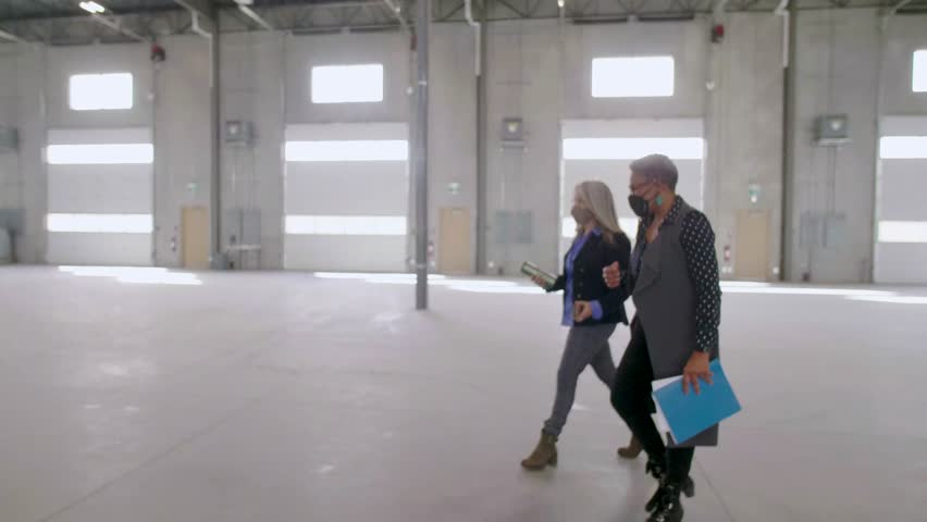 Female architects in face mask talking in empty warehouse loading dock - Powered by Shutterstock - Get 15% off with code: PIKWIZARD15