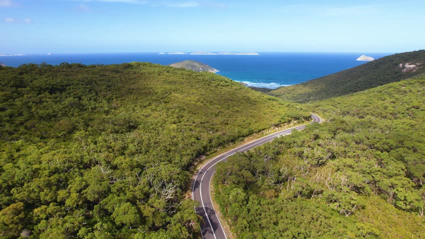 4K drone video of white camper van driving on the road through Wilsons Promontory in Victoria, Australia. The landscapes are lush and green forest with blue vast ocean in the horizon.