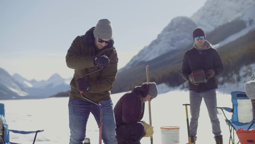 Man drilling into ice on frozen alpine lake