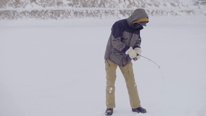Slow motion of man ice fishing on frozen alpine lake