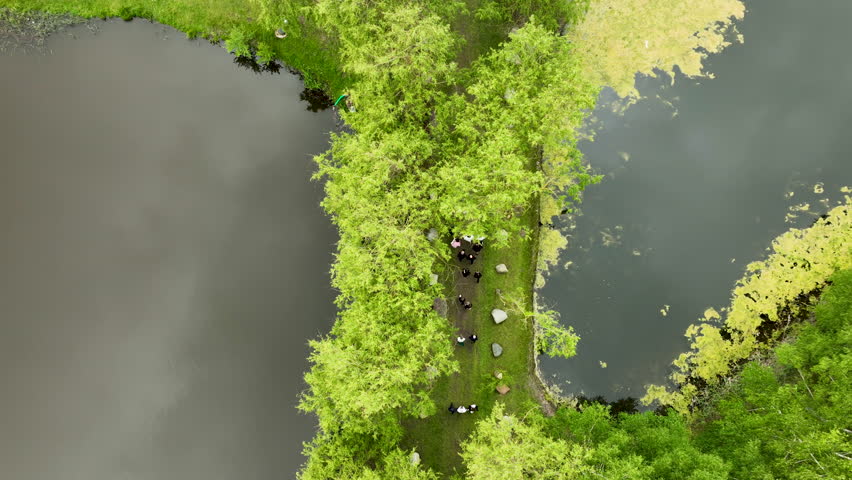 Aerial top-down view of a narrow path through a wooded area between two lakes, showing people walking along the trail.