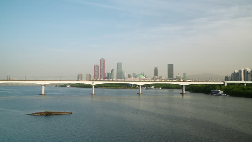 Subway Train Travels on Dangsan Railway Bridge Crosses the Han River in Seoul with Yeongdeungpo District in Background, Sunset Light Reflecting in Moving Train