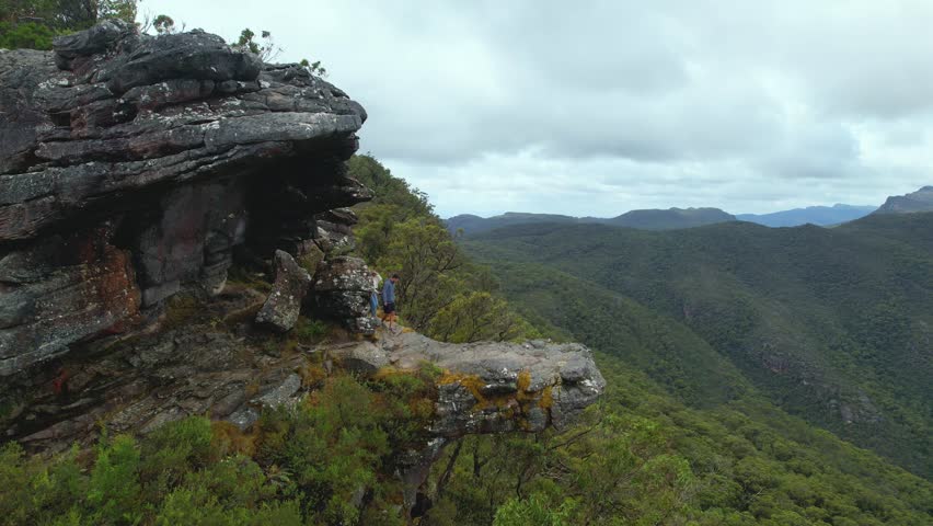 4K Camera Video of couple walking together on the ledge of at The Balconies at The Grampians National Park in Victoria, Australia. The couple enjoy the vast green landscapes and mountain views.