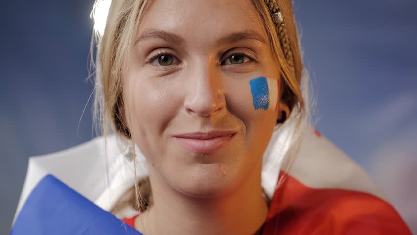 Portrait of France fan. Close up portrait of attractive woman with france flag on shoulder and face, stadium lights in background