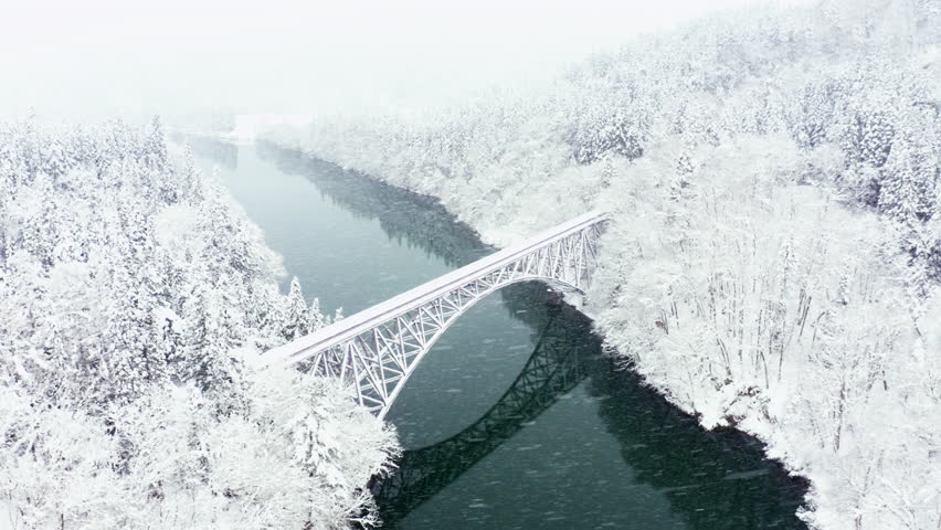 Drone Aerial view Landscape of Railway bridge between the mountain over the river in snow day. Pine tree forest mountain with railroad track covered in snow. Beautiful scenic nature in winter season.