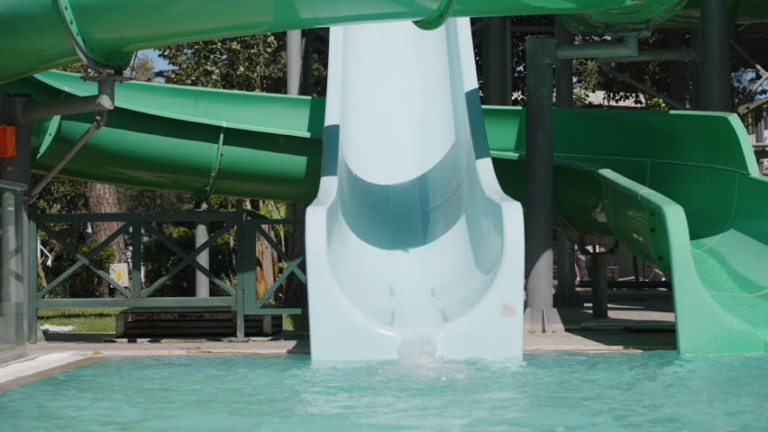 The woman slides down the water slide and glides with splashes into the pool. Camera zooms in. Slow motion. Summer fun.
