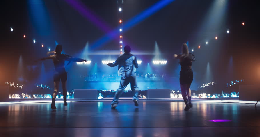 Young K-Pop Singer in Blue Costume Performing a Solo Concert with Show Girls on a Festival Stage. His Charismatic Stage Presence and Lyrics Electrify the Diverse Music Fans in Crowded Arena