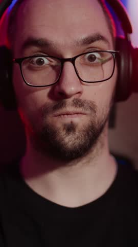 Closeup portrait of funny crazy man listening to music and swaying head like zombie, vertical video. Face of bearded guy with eyeglasses and headphones, hypnotic sound, listen to electronic music