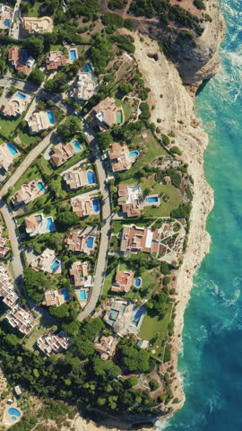 Vertical Screen: Vertical Screen A stunning aerial view reveals oceanfront villas with pools nestled along a picturesque rocky coastline, showcasing luxury homes and dream vacation spots