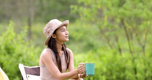 camping woman sit on chair with coffee cup in her hand for drinking in the middle of nature in weekends. 4k video slow motion