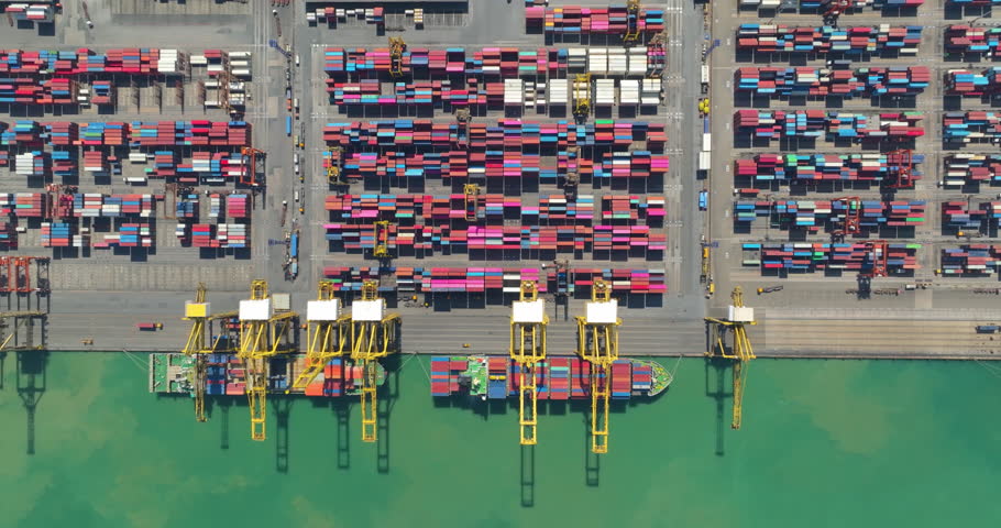 commercial port loading and unloading cargo from container ship import and export by crane for distributing goods by trailers transported to customers and dealers, aerial top down view 4k video