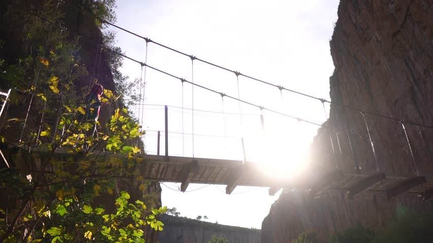 woman stepping over a suspension bridge at sunset, set against huge cliffs