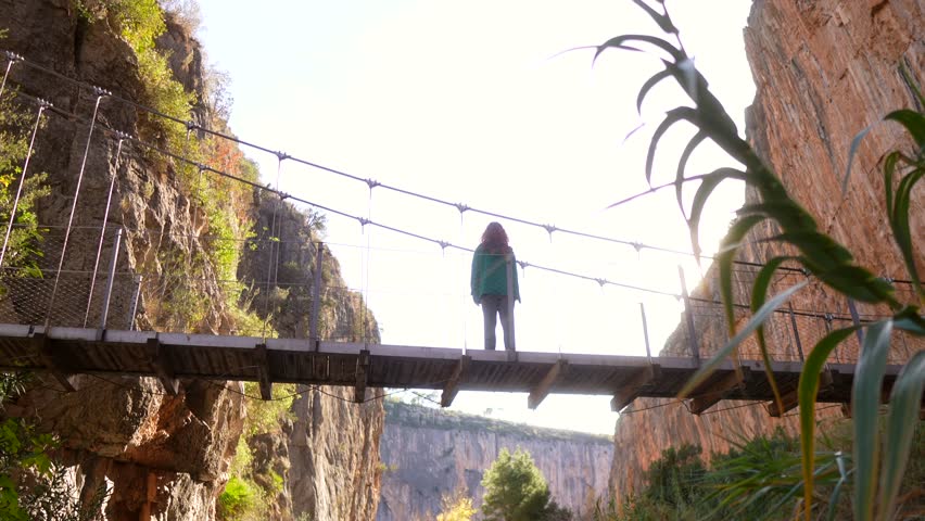 woman spreads her arms and breathes freedom on suspension bridge between cliffs