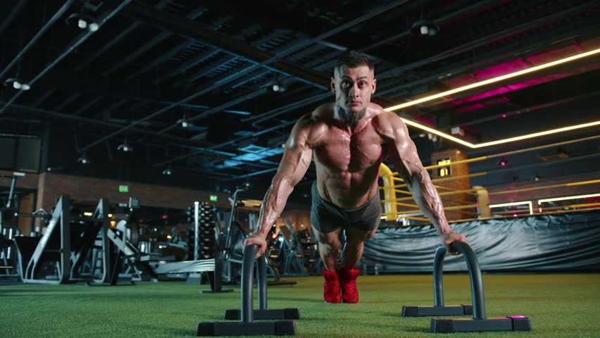 In a contemporary fitness center, a man showcases his commitment to health with rigorous pushup workouts using parallettes, emphasizing strength and dedication to physical wellbeing