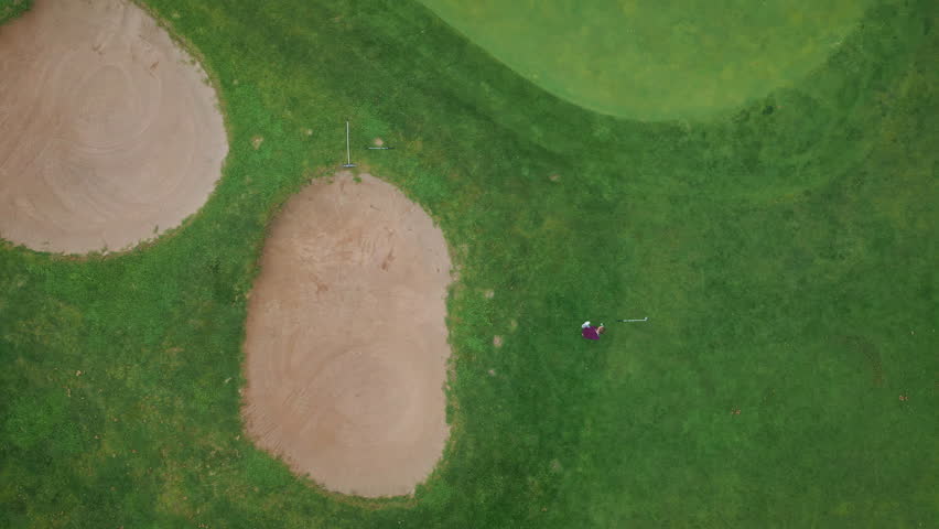 Aerial view golfer take swing on vibrant green course framed by bunkers. Fairways lush grass contrasting with surrounding nature. Greenery covering playfield. Club golf player engaged in calm game.