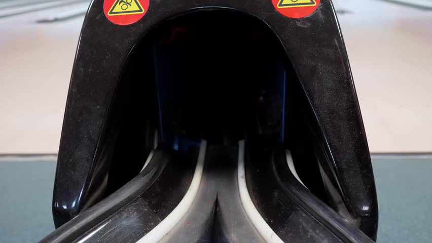 Bowling ball gliding through return rack in action sequence, showcasing essential bowling gear in use.. A Bowling Ball is transitioning from the approach onto the return rack in a bowling alley