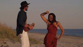 Man playing guitar while woman dances on a sandy beach, enjoying a relaxed and artistic moment by the ocean. A couple enjoys a musical moment on the beach at sunset, with one playing the ukulele and - Powered by Shutterstock - Get 15% off with code: PIKWIZARD15