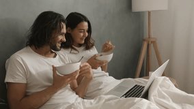 A couple enjoys breakfast in bed while watching something on a laptop, capturing a cozy morning routine. Cinematic slow motion 4k footage, design for advertising, and social media, vlog - Powered by Shutterstock - Get 15% off with code: PIKWIZARD15