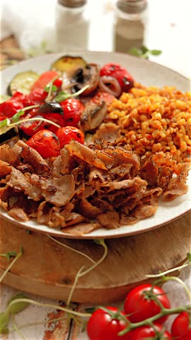 Vertical close up shot of a doner kebab with rice pilaf and grilled vegetables served on a plate. The meal is ready to eat and the table is set. 