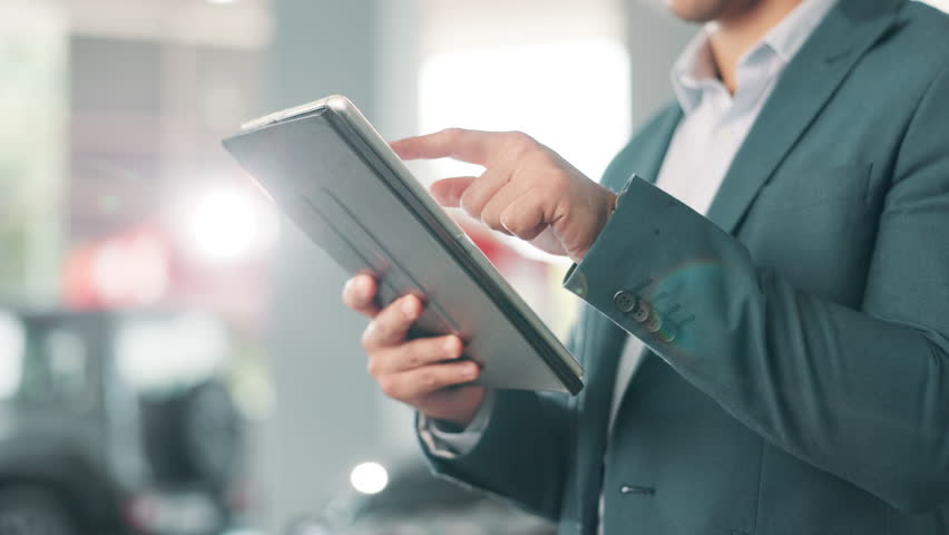 Business, man and typing on tablet at dealership, care sales representative or consultant for inventory information. Person, shop and digital website, choice or online service of vehicle exhibition